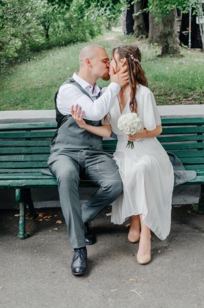Téléchargez les photos : La mariée et le marié baisent assis sur un banc - en image libre de droit
