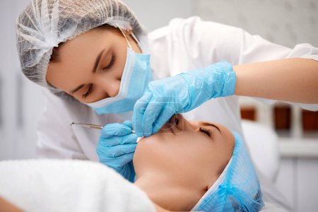 Foto de Mujer joven durante un procedimiento mecánico de limpieza de la cara en la clínica de belleza. Cosmetólogo procedimiento de fabricación para la limpieza de la piel con herramienta de acero de puntos negros y acné - Imagen libre de derechos