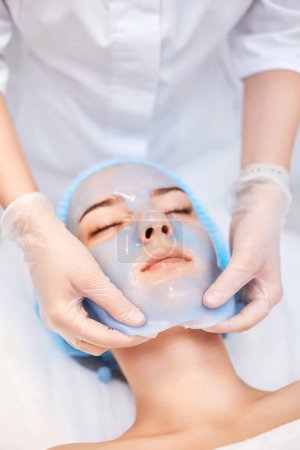 Kosmetikerin entfernt Blaualginatmaske aus dem Gesicht der schönen Frau im Wellness-Salon. Wellnessanwendungen