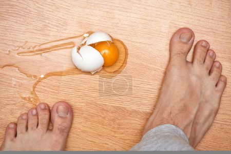 zerbrochenes Ei und Füße auf dem Boden in der Küche, Draufsicht