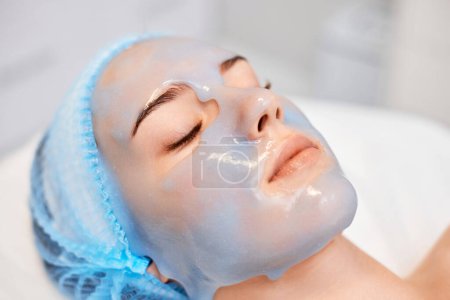 belle femme avec masque en alginate bleu sur le visage dans le salon de spa. gros plan