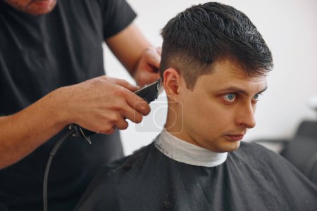 Foto de Corte de pelo con máquina de esquiladora eléctrica en hombre caucásico guapo en la peluquería. - Imagen libre de derechos
