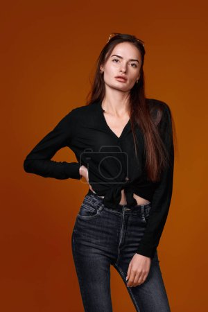Frau in schwarzem Hemd und Jeans auf farbigem Studiohintergrund.