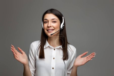 Foto de Mujer sonriente con auriculares está consultando a los clientes en línea sobre fondo gris estudio. Call center, concepto de gente de negocios - Imagen libre de derechos