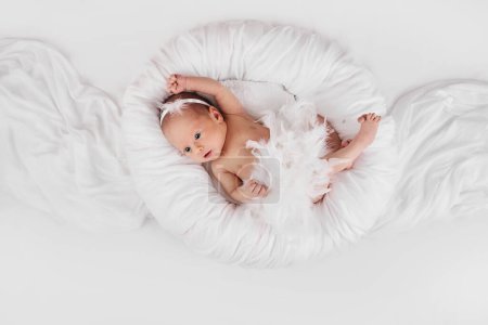 Photo for Sweet newborn baby in dress with feathers in white nest. - Royalty Free Image