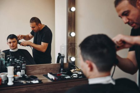 Foto de Hairstylist serving handsome bearded man in barber shop. Haircut in the barbershop. - Imagen libre de derechos