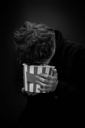 Foto de Portrait of crazy young man holding bucket of popcorn and grimacing . black and white - Imagen libre de derechos