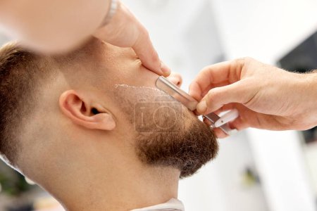 Téléchargez les photos : Barbier rasage homme barbu avec couteau rétro dans le salon de coiffure. gros plan - en image libre de droit