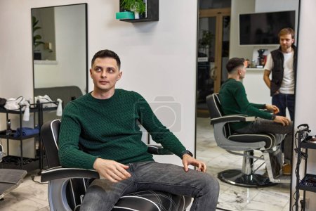 Photo for Satisfied caucasian client man talking with barber while sitting in chair after haircut at barbershop - Royalty Free Image