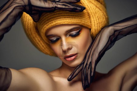 Photo for Beauty elegant blonde model girl with fashionable creative make-up, bright eye line wear yellow turban in black lace gloves on grey background. - Royalty Free Image