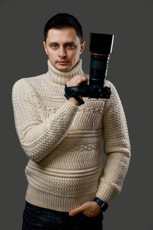 Téléchargez les photos : Jeune photographe professionnel beau en pull avec appareil photo numérique sur fond gris - en image libre de droit
