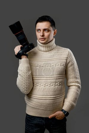 Téléchargez les photos : Jeune photographe professionnel beau en pull avec appareil photo numérique isolé sur fond gris - en image libre de droit
