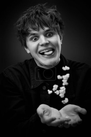 Foto de Portrait of crazy young man throwing up popcorn and grimacing . black and white - Imagen libre de derechos