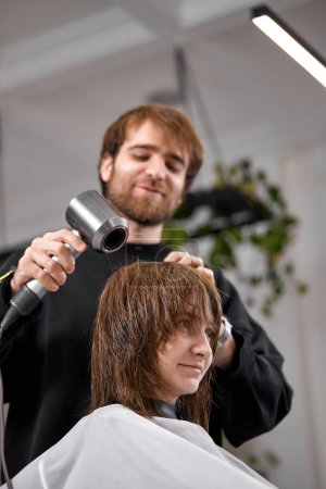 Photo for Man hairdresser using hair dryer for female hair after washing in the beauty salon. - Royalty Free Image