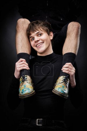 Téléchargez les photos : Young handsome guy hugs male legs in bright shoes on black background. fashion - en image libre de droit