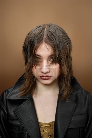 Téléchargez les photos : Jeune femme avec un maquillage lumineux et coiffure élégante en veste noire sur fond beige. - en image libre de droit