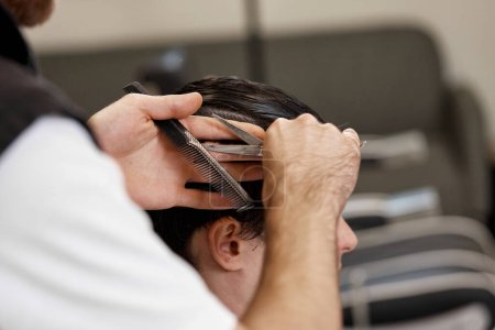 Téléchargez les photos : Close-up, professional hairstylist does haircut for caucasian client man at barber shop. - en image libre de droit