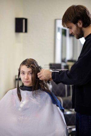 Téléchargez les photos : Male hairdresser is combing the hair of the female client. hairdresser doing hair to his client woman - en image libre de droit