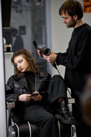 Photo for Man hairdresser using hair dryer for female hair after washing in the beauty salon. - Royalty Free Image