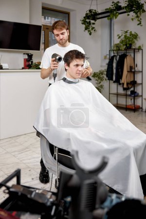 Photo for Professional hairdresser during work with man client with hair dryer in barber shop. Haircut in the barbershop. - Royalty Free Image