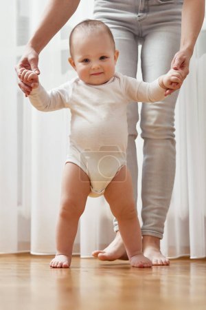 Photo for Happy little baby girl learning to walk with mother help at home. child take her first steps - Royalty Free Image