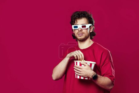 Photo for Handsome bearded man in 3d glasses holding big bucket of popcorns on magenta background - Royalty Free Image