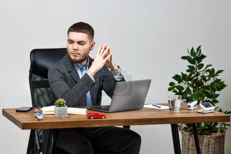 Téléchargez les photos : Jeune homme assis sur une chaise à table et se reposant, en utilisant un ordinateur portable sur fond de mur blanc - en image libre de droit