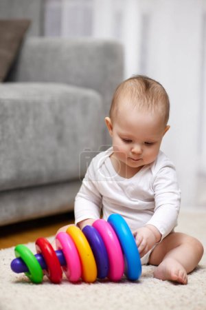 Photo for Cute baby girl playing with colorful toy pyramid sitting on carpet at home. Early development for kids. - Royalty Free Image