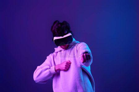 Foto de Hombre en sudadera con gafas de realidad virtual sobre fondo azul. Iluminación neón - Imagen libre de derechos
