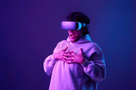 Foto de Man in sweatshirt using virtual reality glasses on blue background. Neon lighting - Imagen libre de derechos