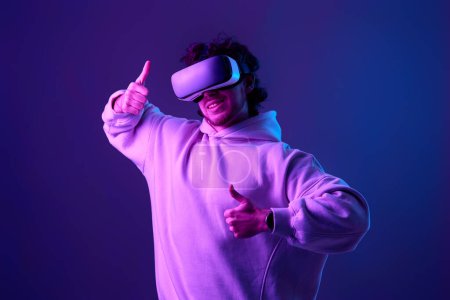 Photo for Man in sweatshirt using virtual reality glasses and playing video games on blue background. Neon lighting - Royalty Free Image