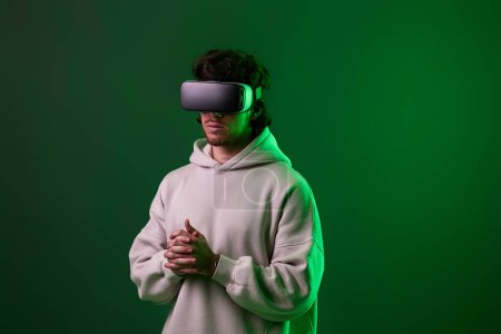 Photo for Man in sweatshirt using virtual reality headset on green background. Neon lighting - Royalty Free Image