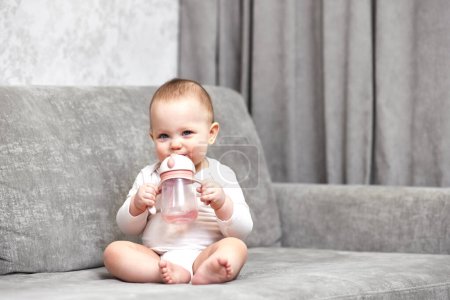 Photo for Cute baby girl holding bottle and drinking water at home. - Royalty Free Image