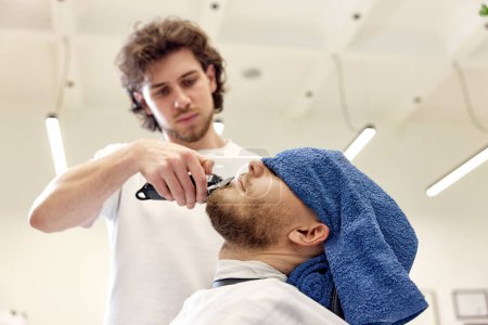 Photo for Barber shaving handsome bearded man in barber shop. - Royalty Free Image