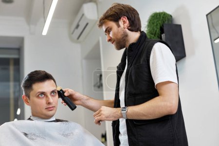 Téléchargez les photos : Barber cut hair with electric shearer machine on man in barber shop. - en image libre de droit