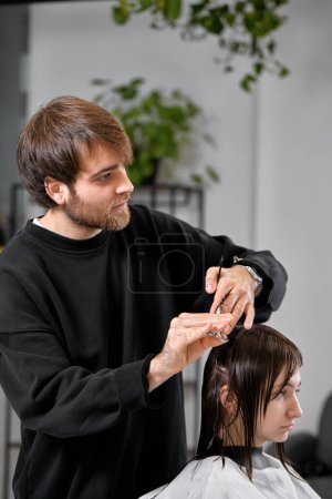 Photo for Professional male hairdresser with scissors cutting female hair in salon - Royalty Free Image