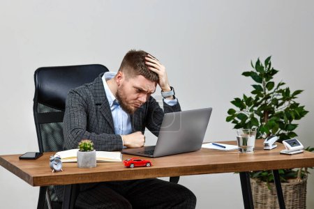 Photo for Young man using laptop, sitting on chair at desk, having problems thinking about troubles - Royalty Free Image