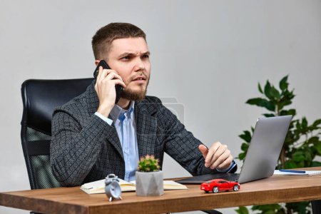 Photo for Businessman working with laptop and having phone conversation with client - Royalty Free Image