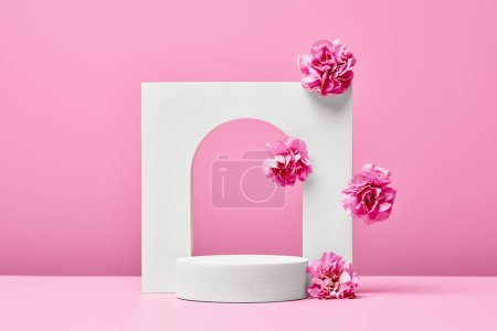 Téléchargez les photos : Podium blanc avec des fleurs roses et arc élégant isolé sur fond rose pastel. étape de présentation des produits cosmétiques - en image libre de droit