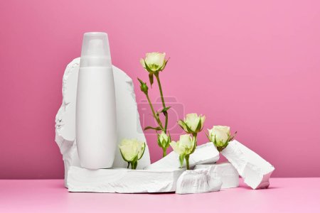 Téléchargez les photos : Bouteille blanche de crème ou lotion pour le corps avec pierres et roses blanches isolées sur fond rose - en image libre de droit