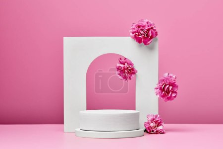 Téléchargez les photos : Podium blanc avec des fleurs roses et arc élégant isolé sur fond rose pastel. étape de présentation des produits cosmétiques - en image libre de droit
