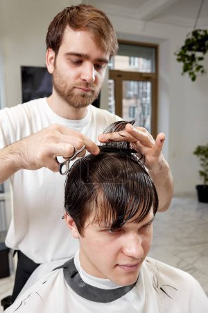 Foto de Professional male hairstylist serving young caucasian client man at modern barber shop. - Imagen libre de derechos