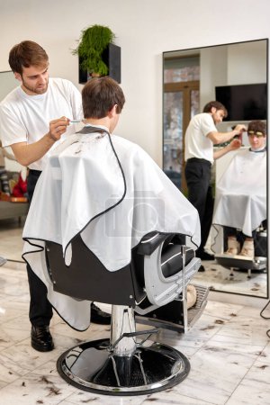 Foto de Young caucasian man getting haircut by professional male hairstylist at barber shop. - Imagen libre de derechos