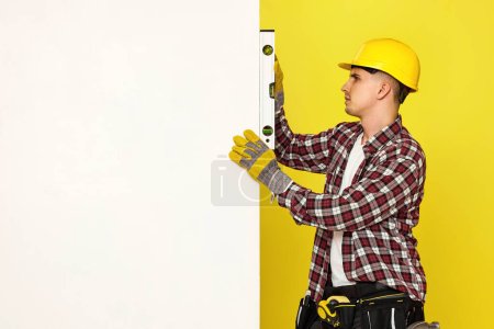 Photo for Professional builder in work clothes in helmet using spirit level and measuring vertical surface. copy space for text - Royalty Free Image