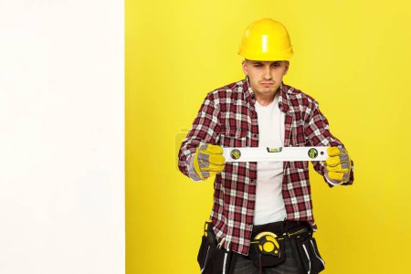 Photo for Professional builder in work clothes in helmet looking at building bubble spirit level . copy space for text - Royalty Free Image