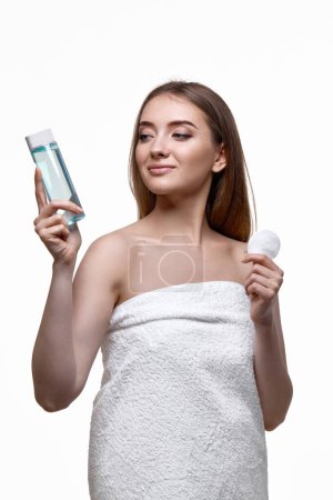 Foto de Hermosa mujer sosteniendo botella con tónico, limpieza de la piel con almohadilla de algodón. Belleza y cuidado de la piel concepto - Imagen libre de derechos
