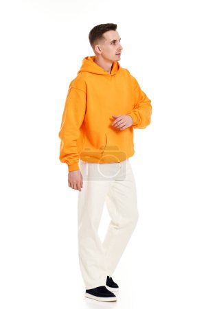 Photo for Young handsome man in orange blank sweatshirt with space for your logo or design on white background. Mockup for print Full length - Royalty Free Image