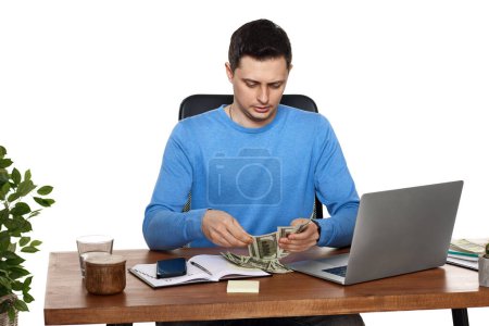 Photo for Positive businessman working on laptop and holding money while sitting on chair at desk. - Royalty Free Image