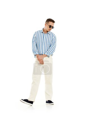 Téléchargez les photos : Jeune homme à la mode en lunettes de soleil à la mode, chemise à rayures bleues et pantalon isolé sur fond blanc. longueur totale. - en image libre de droit
