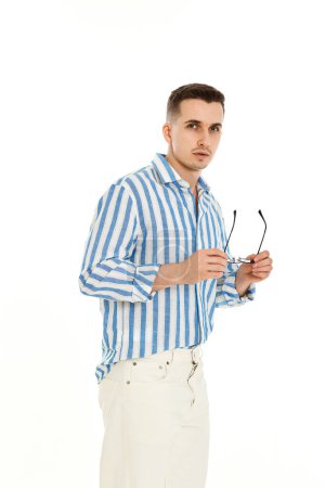 Foto de Joven guapo en gafas de sol y camisa de rayas azules aislado sobre fondo blanco. Moda de verano - Imagen libre de derechos
